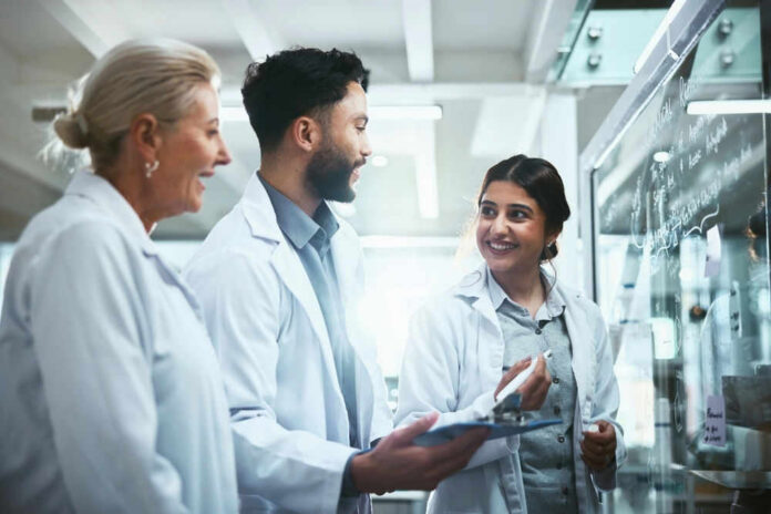 Three scientists discussing work at a glass board