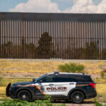 High-Tech Defenses: The New Border Strategy Police vehicle parked in front of tall fence.