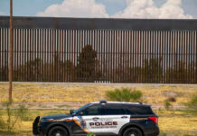 Police vehicle parked in front of tall fence.