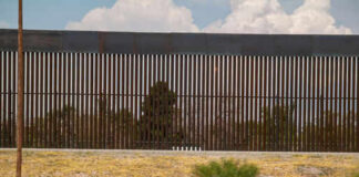 Police vehicle parked in front of tall fence.
