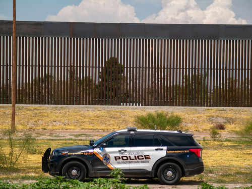 Police vehicle parked in front of tall fence.