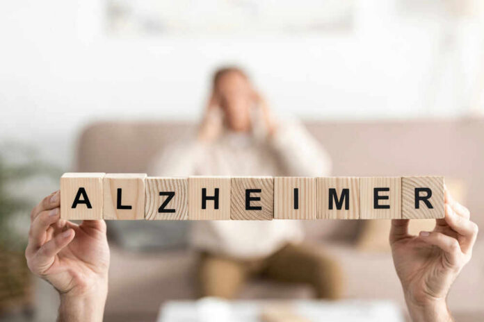 alzheimer-317588180 Wooden blocks spelling Alzheimer with blurred person behind