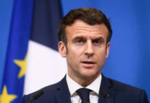 Man speaking at press conference with flags behind