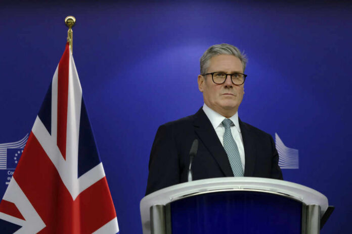 Man in suit at a podium, British flag behind.