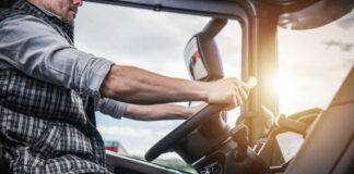 A truck driver gripping the steering wheel inside a vehicle cabin