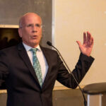 A man in a suit speaking passionately at a podium