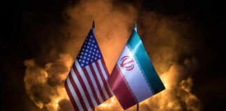 Flags of the United States and Iran displayed on stands with a smoky background
