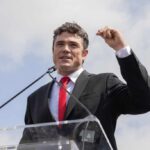 FBI PROBES Trump Appointee Over Classified Leaks A man in a black suit and red tie speaking at a podium outdoors