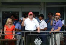 Group of people at a golf event with a political figure in a red hat