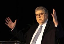A man in a suit gesturing while speaking at a podium