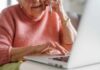 Elderly woman talking on the phone while using a laptop