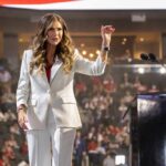 A woman in a white suit speaking at a podium during a conference