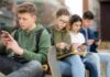 OUTRAGE! Kids Still Vulnerable – UK Ban Fails Group of teenagers sitting outdoors, focused on their devices