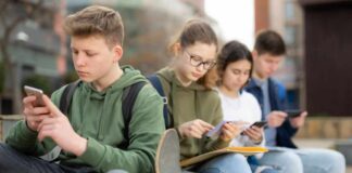 Group of teenagers sitting outdoors, focused on their devices