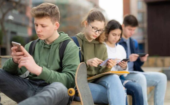 shutterstock_2573783959.jpg Group of teenagers sitting outdoors, focused on their devices