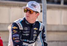 Race car driver wearing sunglasses and a team uniform, sitting outdoors