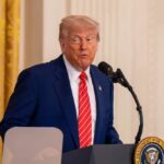 Trump’s Mail-In Voting CRACKDOWN Sparks National Uproar A man in a suit speaking at a podium in a formal setting