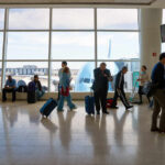 DHS Shutdown Sparks Airport Collapse Fears Passengers in an airport terminal with luggage and an airplane visible outside