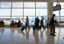 Passengers in an airport terminal with luggage and an airplane visible outside