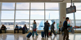 Passengers in an airport terminal with luggage and an airplane visible outside
