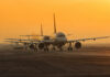 Airplanes lined up on a runway during sunset