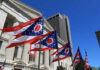 Ohio state flags waving in front of a government building under a clear blue sky