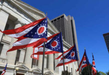 Ohio state flags waving in front of a government building under a clear blue sky
