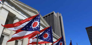 Ohio state flags waving in front of a government building under a clear blue sky