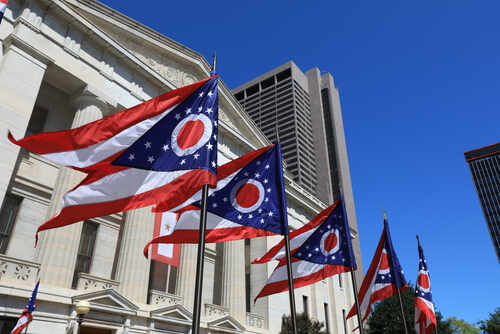 Ohio state flags waving in front of a government building under a clear blue sky