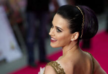 A woman with dark hair styled in an elegant updo smiles at the camera on a red carpet