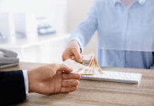 A person handing over cash through a transparent barrier at a bank counter