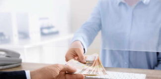 A person handing over cash through a transparent barrier at a bank counter