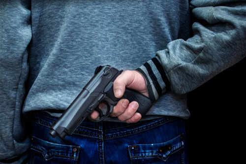 shutterstock_1218320311.jpg Person holding a handgun behind their back