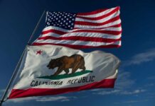 American and California flags waving against a blue sky