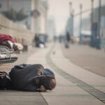 A person lying on the ground in a city street, with benches nearby