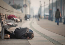 A person lying on the ground in a city street, with benches nearby