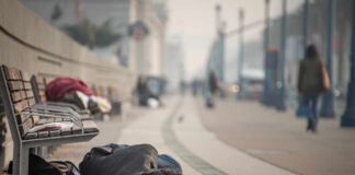 A person lying on the ground in a city street, with benches nearby