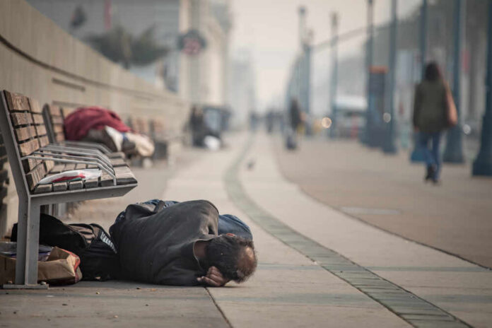 A person lying on the ground in a city street, with benches nearby