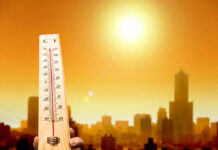 Thermometer displaying high temperature against a sunset city skyline