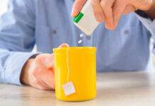 Person adding sweetener to a yellow mug of tea