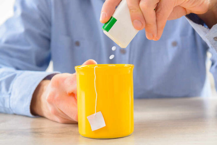 Person adding sweetener to a yellow mug of tea