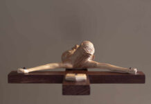 A wooden sculpture of a figure with outstretched arms on a wooden base