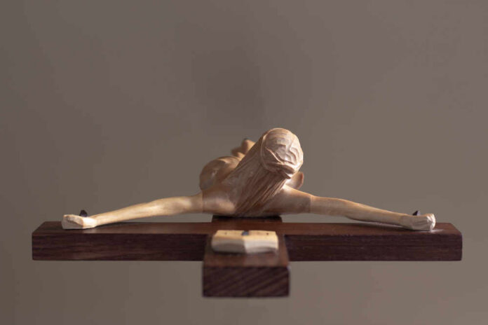 A wooden sculpture of a figure with outstretched arms on a wooden base