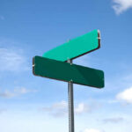 Two blank green street signs against a blue sky