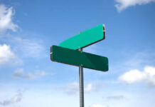Two blank green street signs against a blue sky