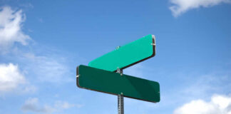Two blank green street signs against a blue sky