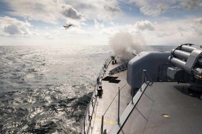 Naval ship firing a weapon into the ocean with a plane flying overhead