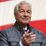A business leader applauding at an outdoor event with an American flag in the background