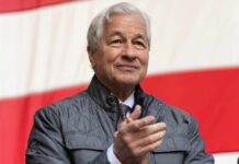 A business leader applauding at an outdoor event with an American flag in the background