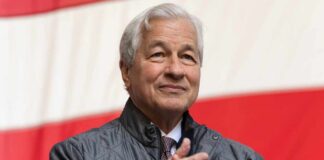 A business leader applauding at an outdoor event with an American flag in the background